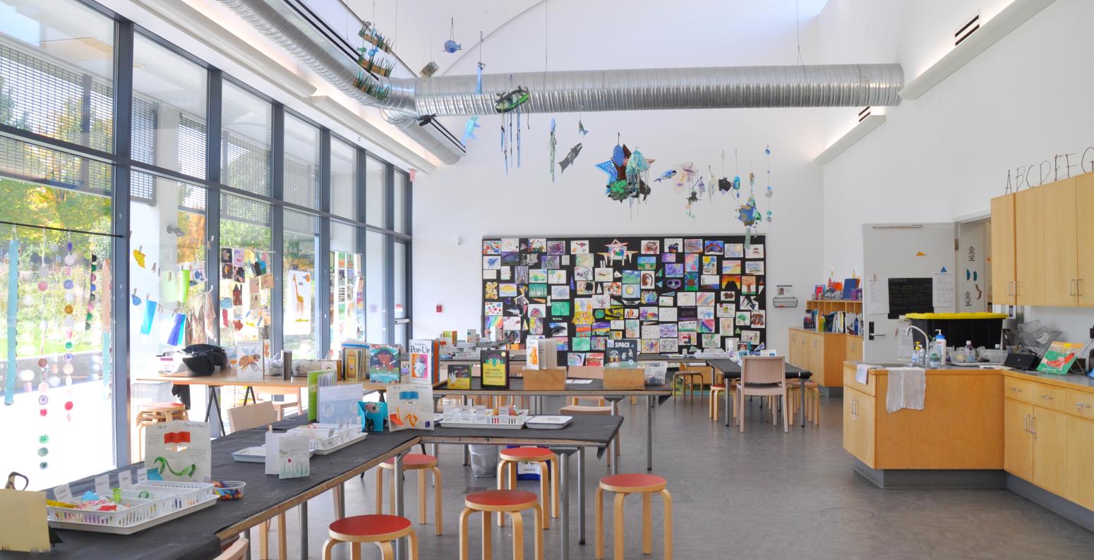 An open Art Studio with artworks on display, stools and chairs, and bright light streaming through the windows.