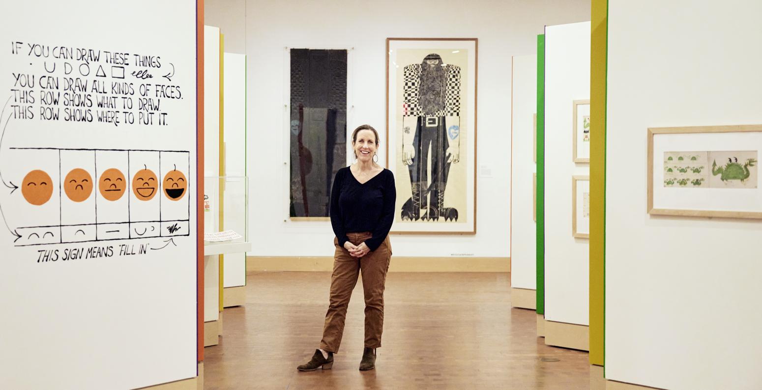 Alix Kennedy standing in gallery at The Carle with Ed Emberley artwork in background