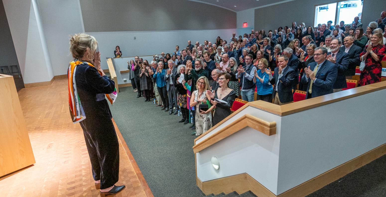 A woman stands on the stage watching as the crowd gives her a standing ovation.