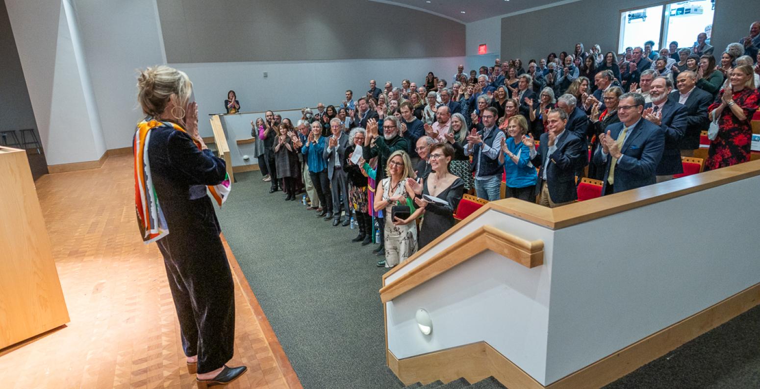 A woman stands on the stage watching as the crowd gives her a standing ovation. 