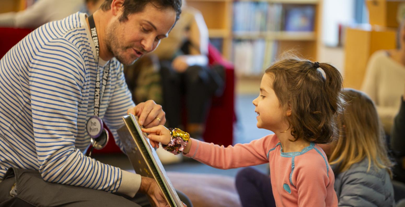 Child pointing at book held by Carle educator.