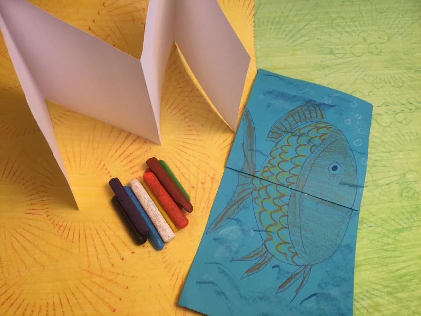 Accordion-fold books laid next to crayons and on top of textured papers