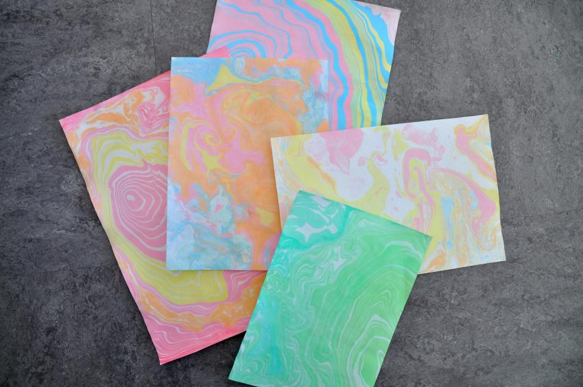 Five papers that have been marbled with the suminagashi technique, with concentric circles and swirls of color.