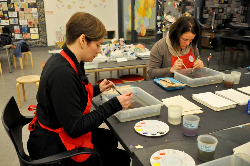 Two adults carefully dipping brushes with ink onto the surface of water.