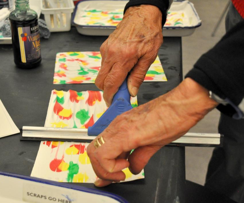 A squeegee is pulled across a paper to reveal a brightly-colored, marbled paper.