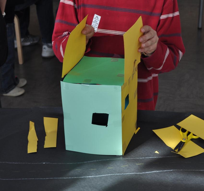 A child making a house out of yellow and green paper. 