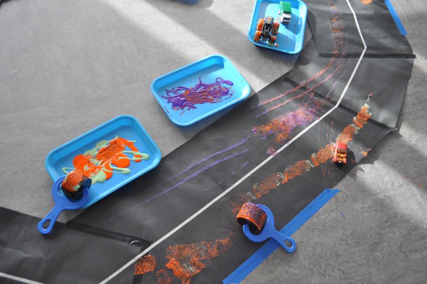 An oval track shape made from black paper, with toy trucks and trays of paint. 
