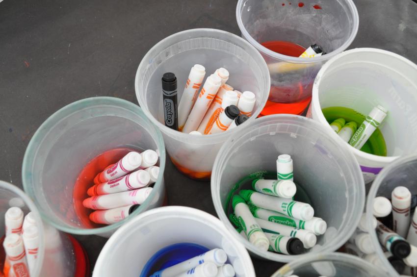 Cups of markers sorted by color soaking in water.