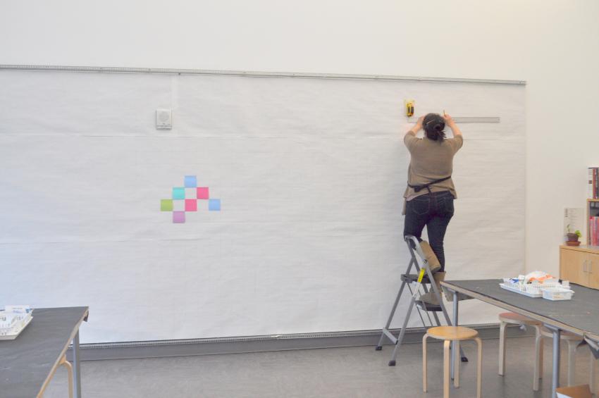 A volunteer installing Post-Its onto a mostly white display wall. 