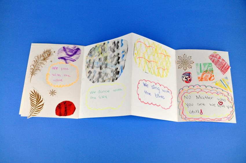 An accordion fold book unfolded to show four pages with collage, drawings, and words.