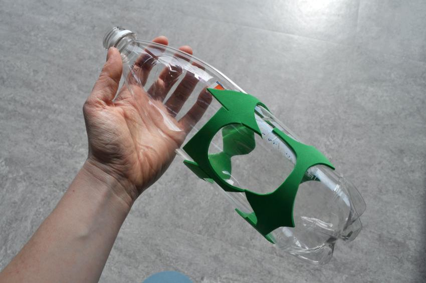 A hand holds a large bottle that is covered in soft, plastic foam pieces.