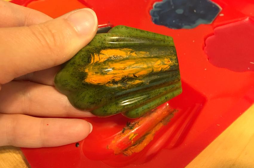 A green crayon lifted out of the mold to reveal yellow swirls on the top of the crayon.