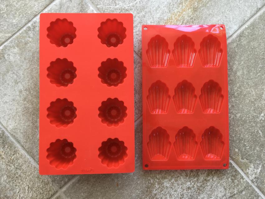 Two red silicone molds used for baking canelé pastries and madeleine cookies.