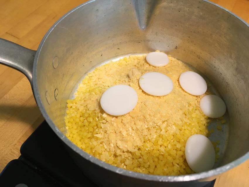 Wax pellets and cocoa butter coins sitting in a silver pot on a scale.