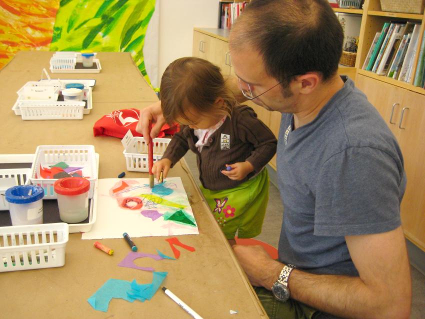 An adult and child work together to create a collage using tissue paper and liquid starch glue.