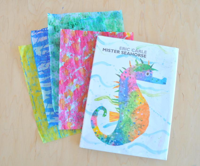 The book Mr. Seahorse by Eric Carle on top of a stack of watercolor-painted papers.