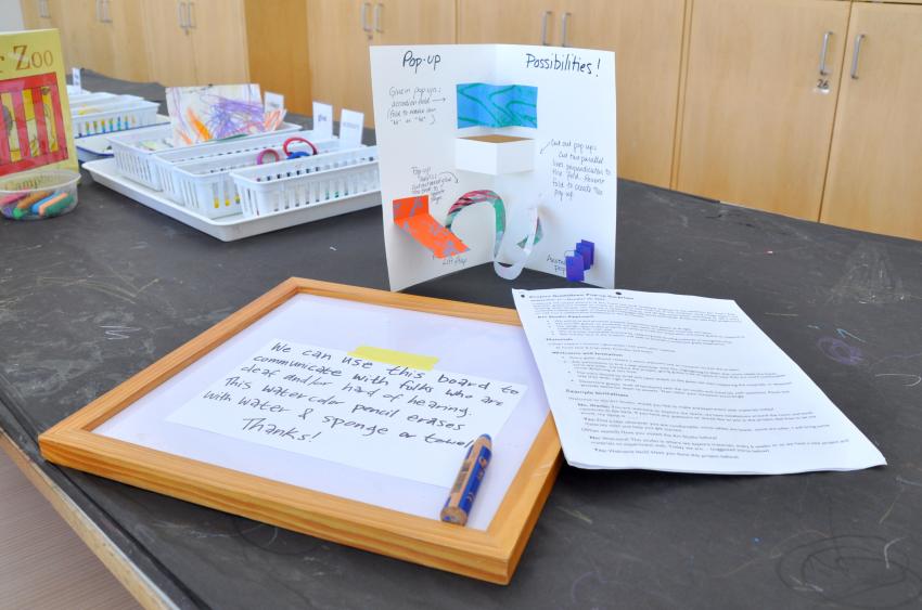 A pop-up card with ideas on how to make pop-ups, a white board with a note suggesting how staff can use it to communicate with guests, and an intro pack with more information about the project.