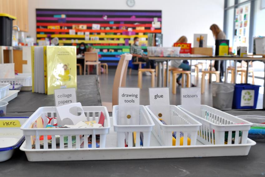 A tray of materials on a table with a colorful Art Studio in the background.