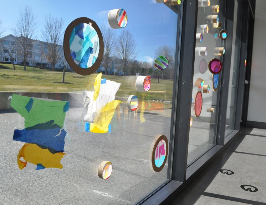 Colorful tissue paper collages on contact paper shine brightly in a window display.