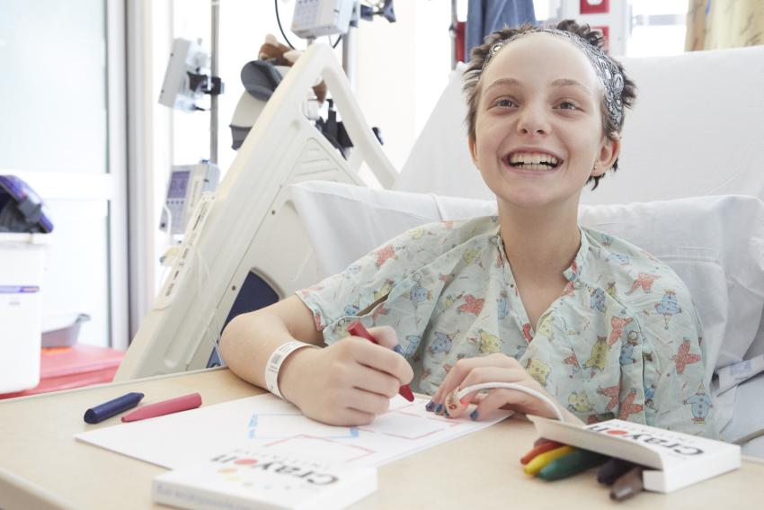 A child in a hospital bed smiles brightly while drawing with crayons from The Crayon Initiative.