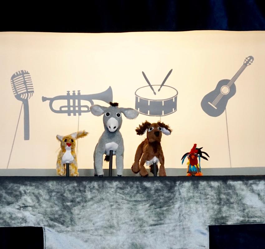Four animal puppets on stage in front of silhouettes of musical instruments.