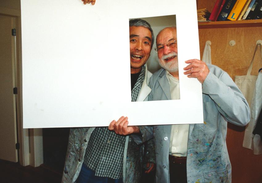 Photograph of Eric Carle and Kazuo Iwamura with faces in book cutout. 