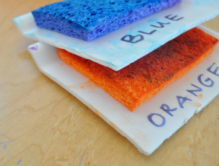Two stamp pads stacked on top of one another, the top one with blue tempera paint and the bottom with orange tempera paint. 