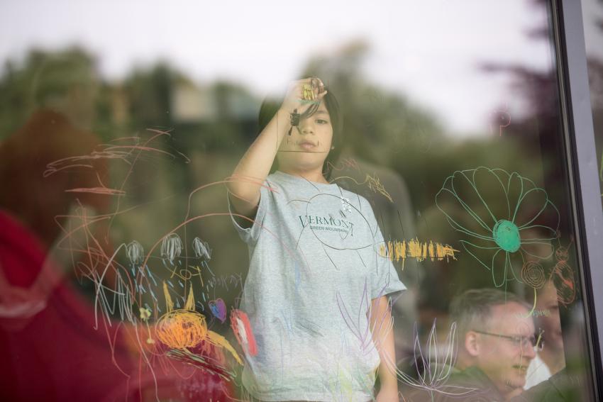 A child focuses and draws on a window pane with a watercolor pencil.