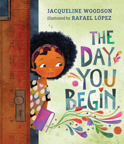 A dark skinned girl with curly black hair peers nervously around a classroom door carrying a book.