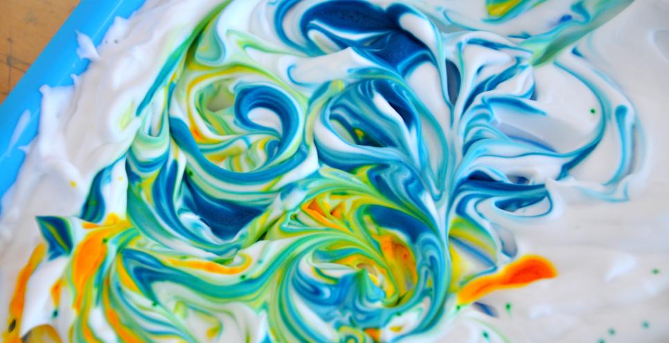 Blue and yellow swirls of color within white shaving cream.
