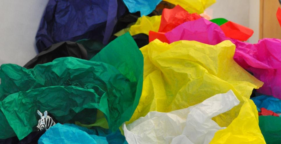A pile of brightly colored tissue paper cascading off a wall and onto the floor with a hidden zebra beneath the folds.