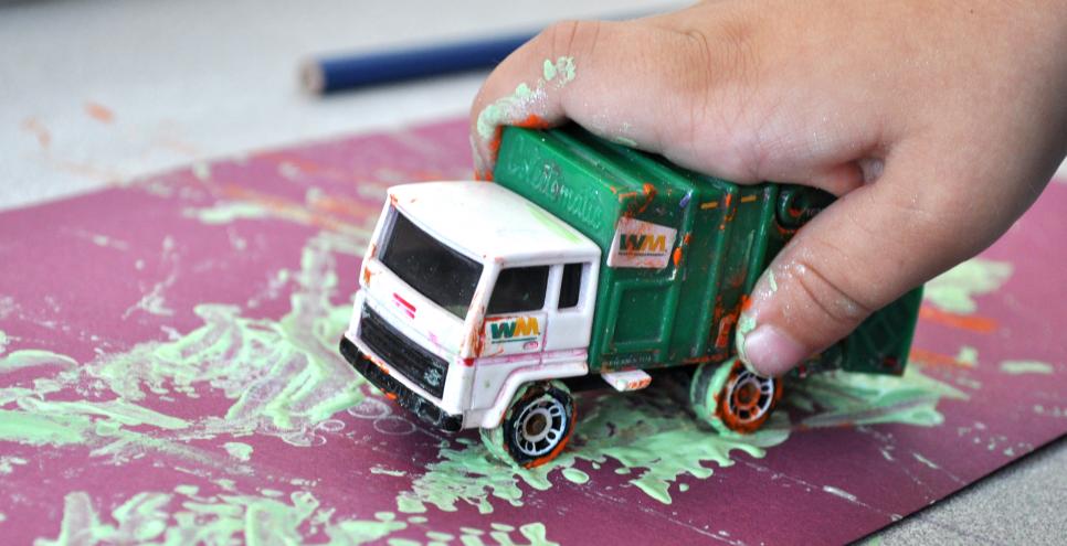 Photograph of child painting with toy truck.
