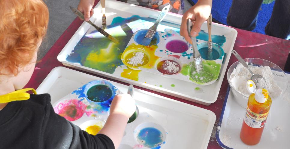 Young painters dipping brushes into colorful palettes.