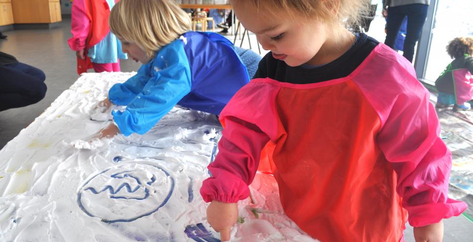 Two young children making marks into shaving cream on a table.