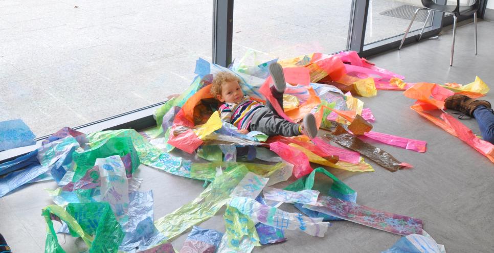 A young child playing within a pile of colorful papers on the ground.