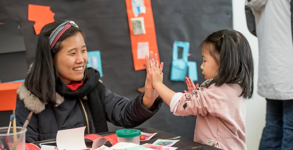 adult and child give high fives while making art in the art studio at The Carle