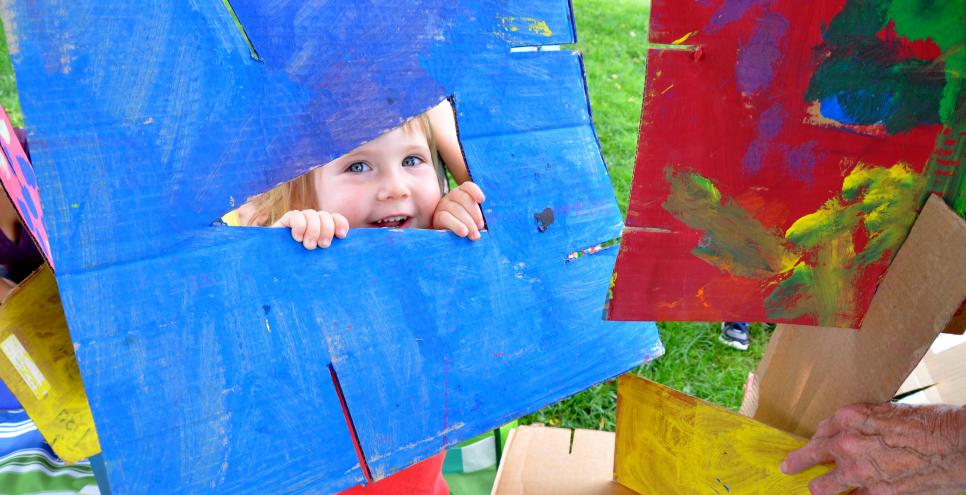 A child smiling through a brightly-painted piece of cardboard.