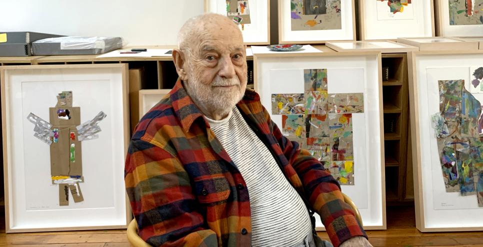 Eric Carle sitting in studio with framed Angels. 