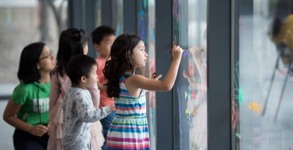 Children writing with Stabilo watercolor pencils on a large window.