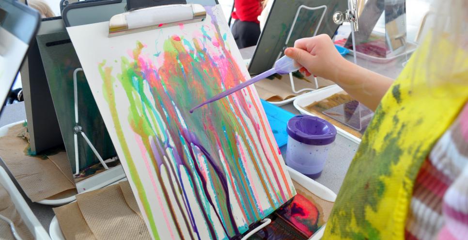 A toddler painting with a dropper and liquid watercolor onto a vertical piece of paper clipped into a clipboard.