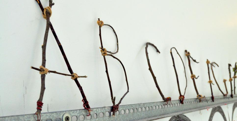 An alphabet made from twigs and twine attached to a long metal rail.