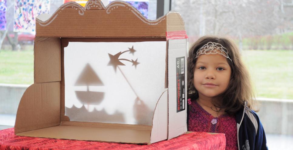 A child playing with a shadow puppet theater made from a copy paper box.