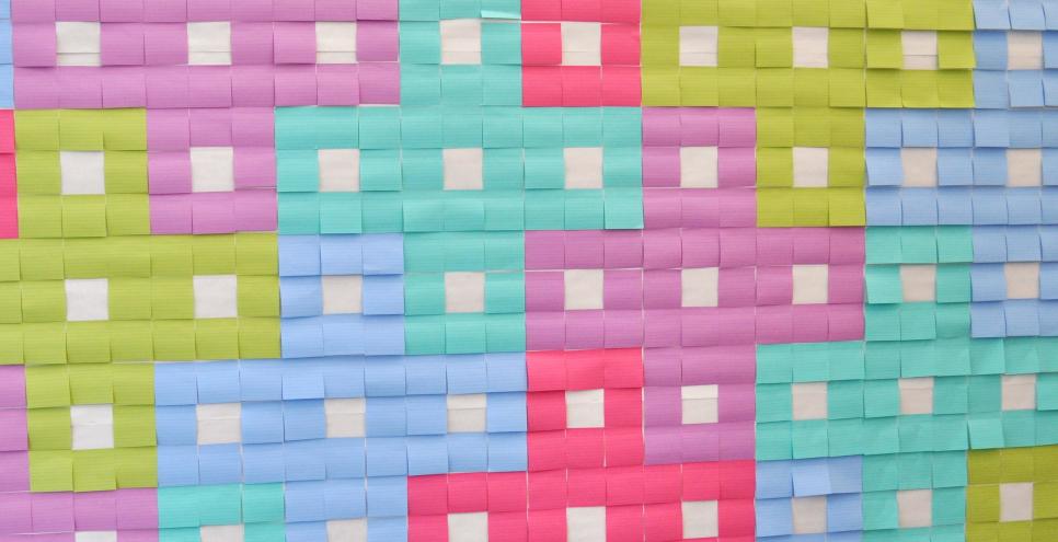 A wall covered in blank, colorful sticky notes creating a pattern.