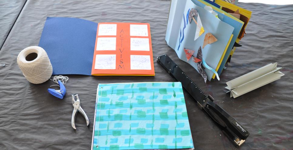 Three examples of books made from past Everyday Art Projects, accompanied by string, two-hole punchers, a crown binding, and a long reach stapler.  