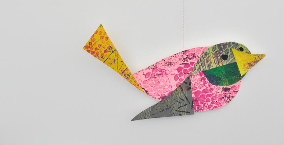 A mobile with one colorful collage bird hanging from a wooden twig.