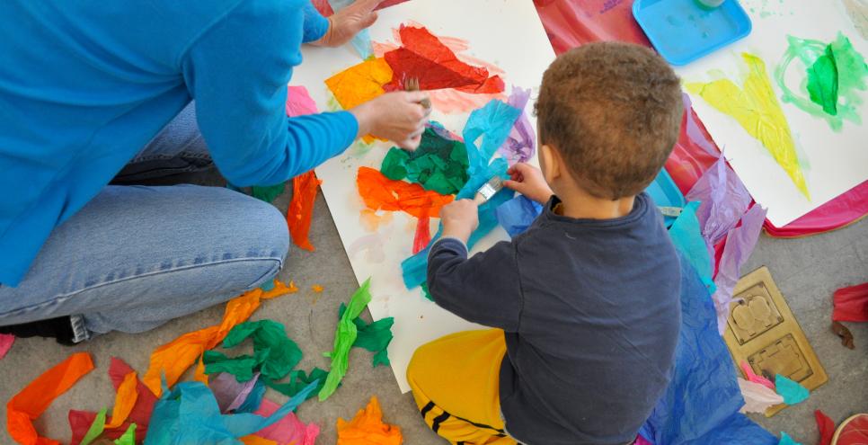 A child gluing tissue paper onto a large watercolor paper. 