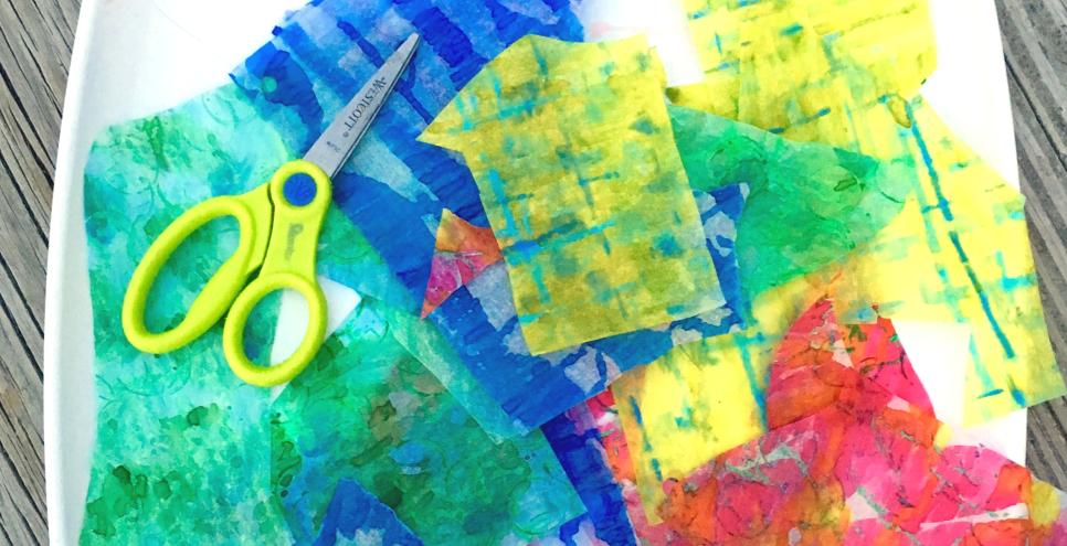 A tray with pieces of watercolor-painted papers and a pair of scissors.
