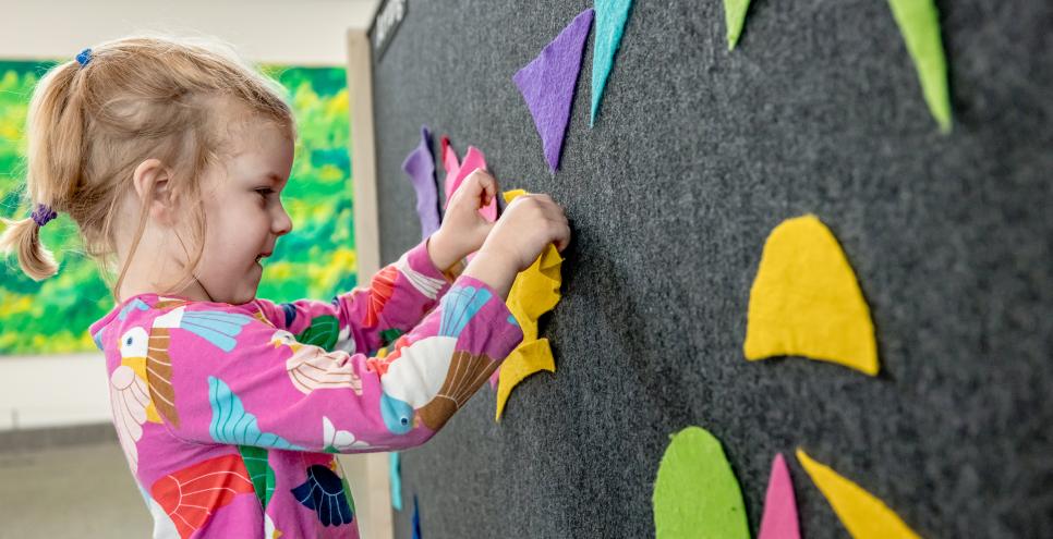 child arranging colorful pieces of felt on a large board with Eric Carle's mural in the background