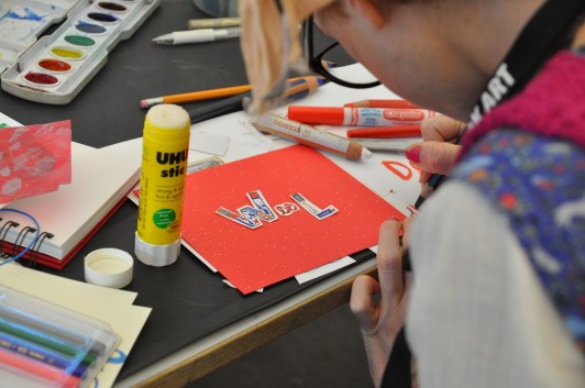 Participant working on an artwork where the word "Wool" is partially cut from collage papers and partially written.