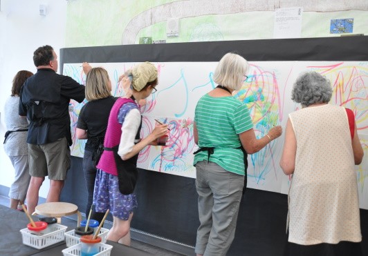 Participants standing in front of the wall and painting the large watercolor paper.